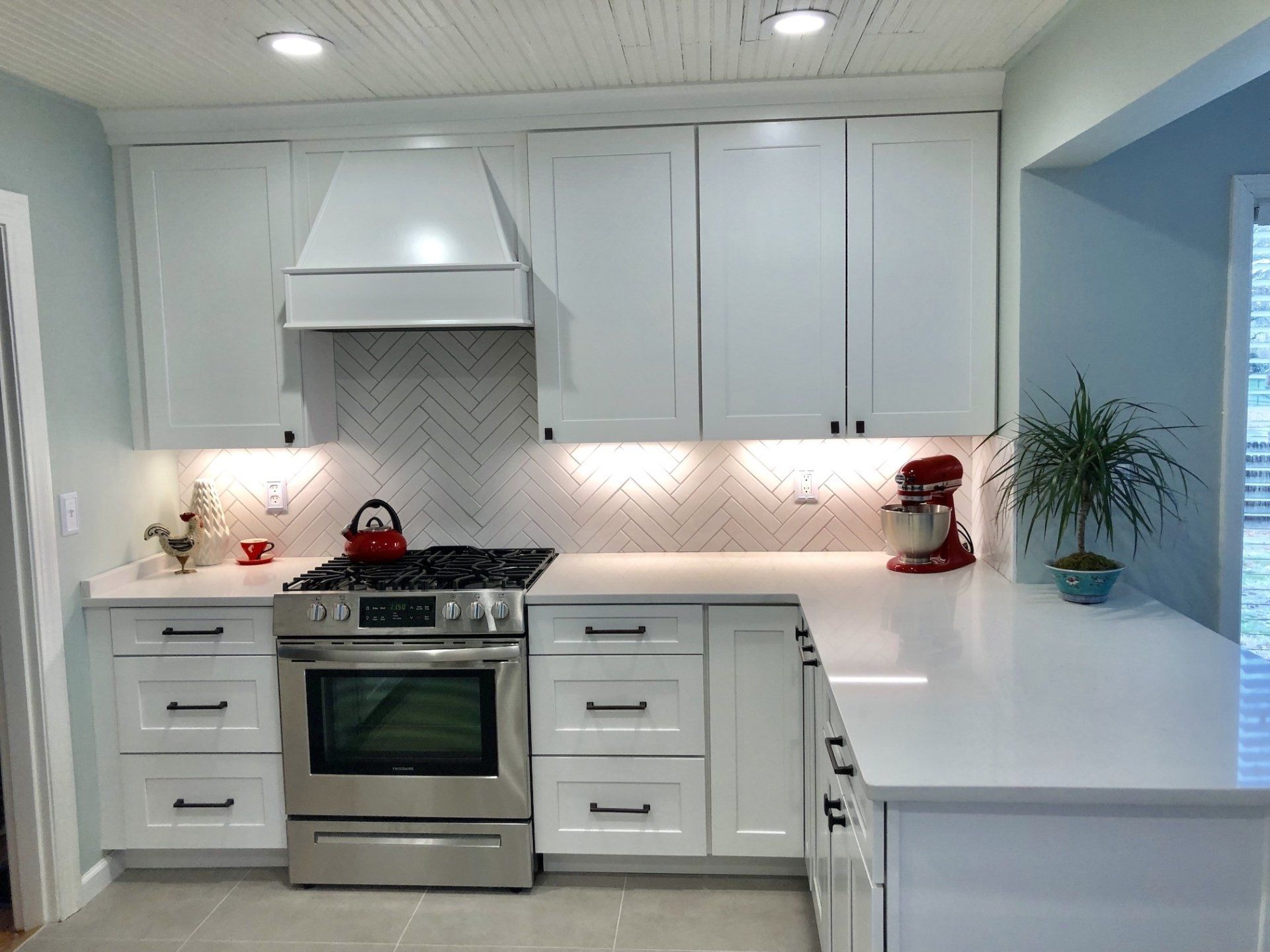 White kitchen with light blue walls, white cabinets, stainless steel stove, and herringbone backsplash.
