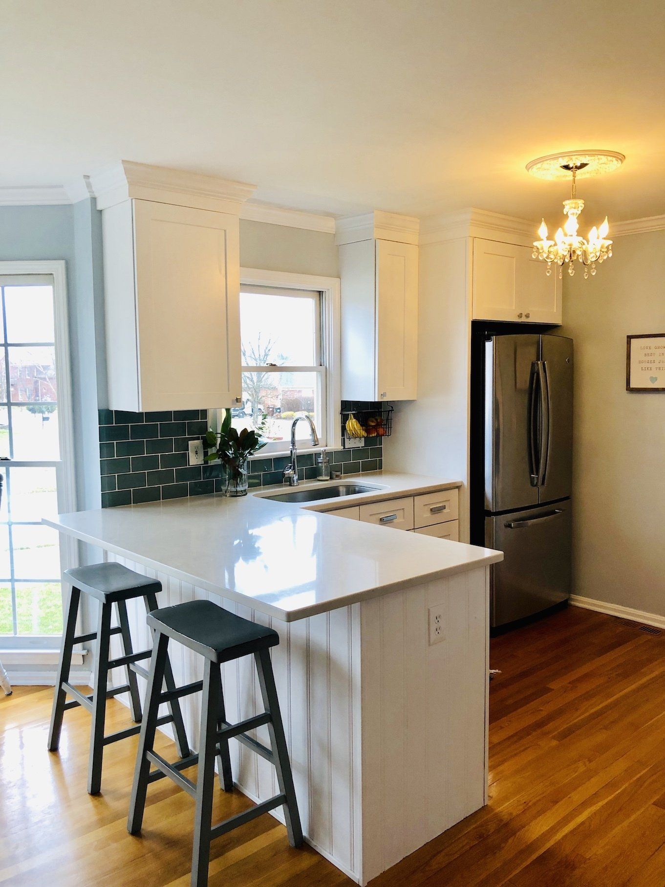 Modern kitchen with white cabinets, stainless steel refrigerator, and a white countertop island with two stools.