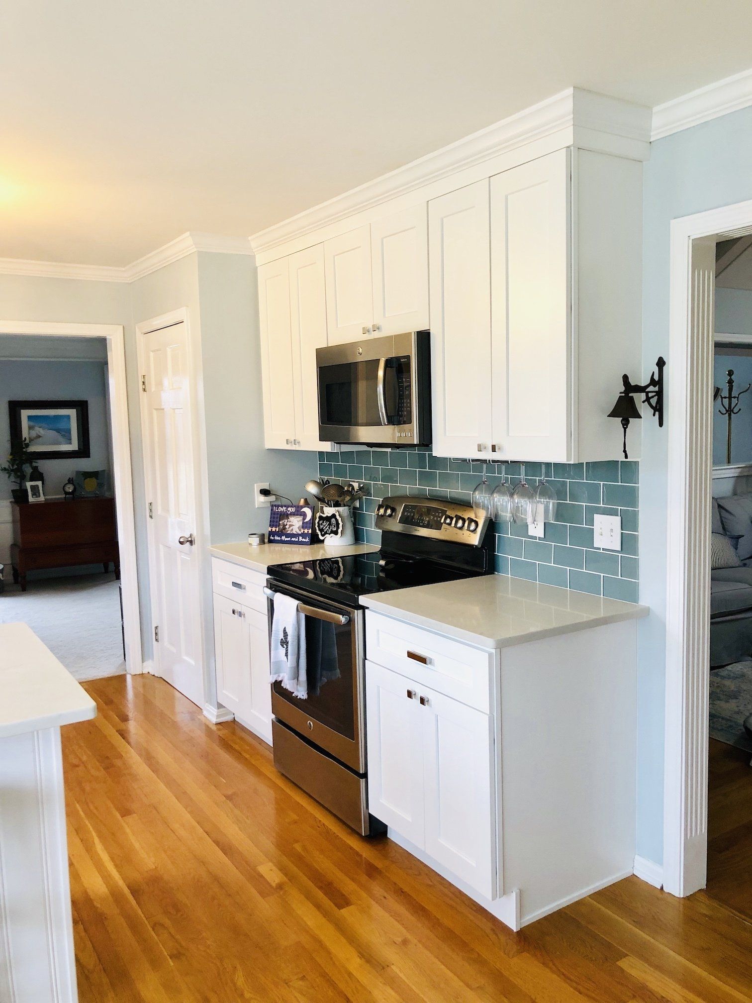 White kitchen with stainless steel appliances, blue tile backsplash, and light wood floor.