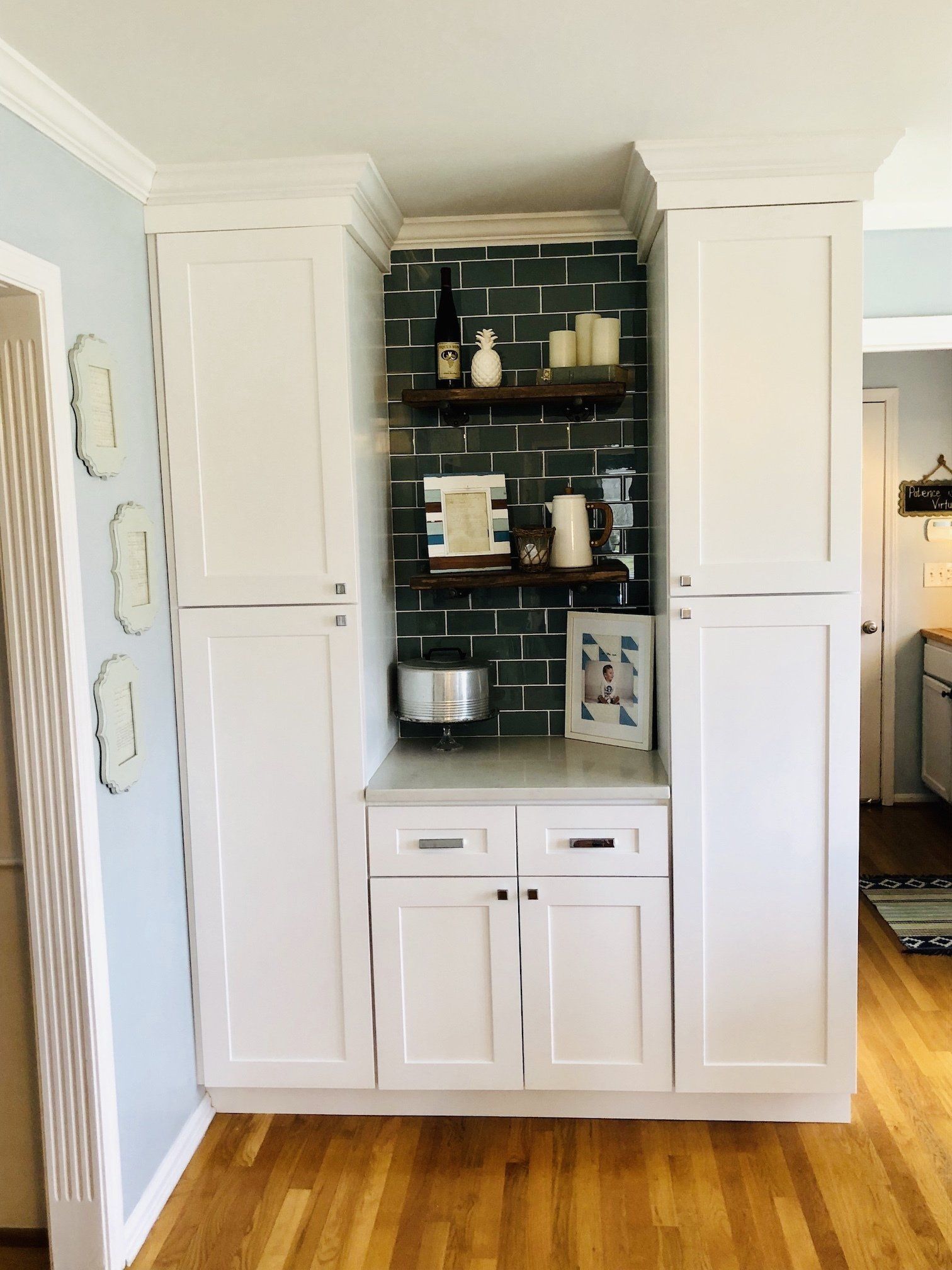 White built-in kitchen cabinet with coffee station. Green tile backsplash, wooden shelves, and a small appliance.