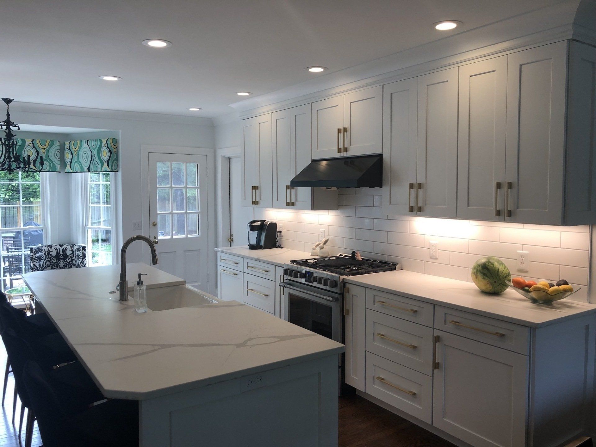 White kitchen with island, cabinets, stove, and a window with green patterned shade.