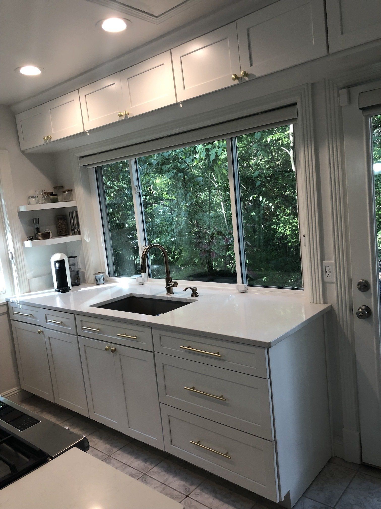 White kitchen with upper and lower cabinets, large window, and gold hardware.