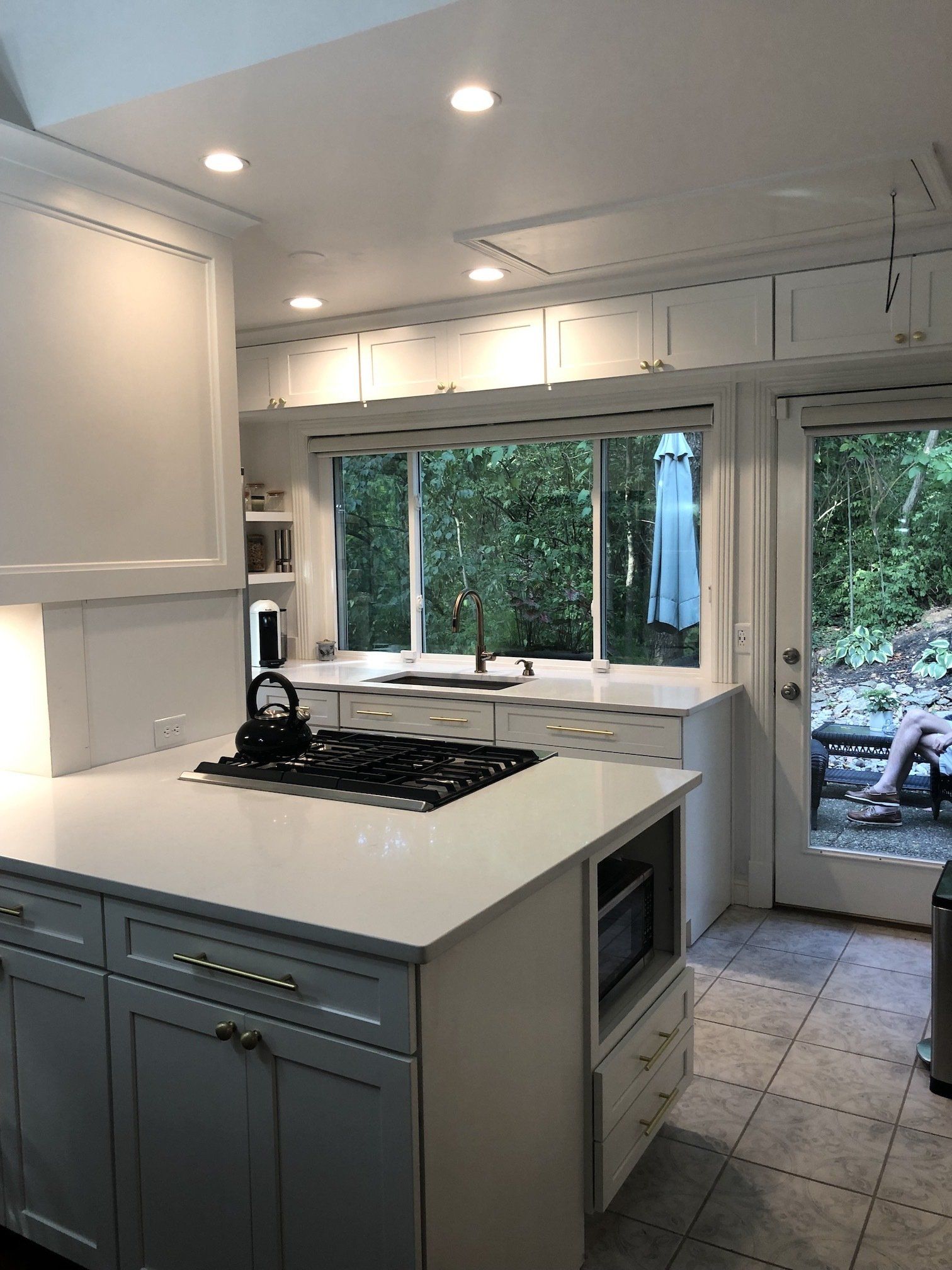 White kitchen with island, cooktop, and window looking onto greenery.