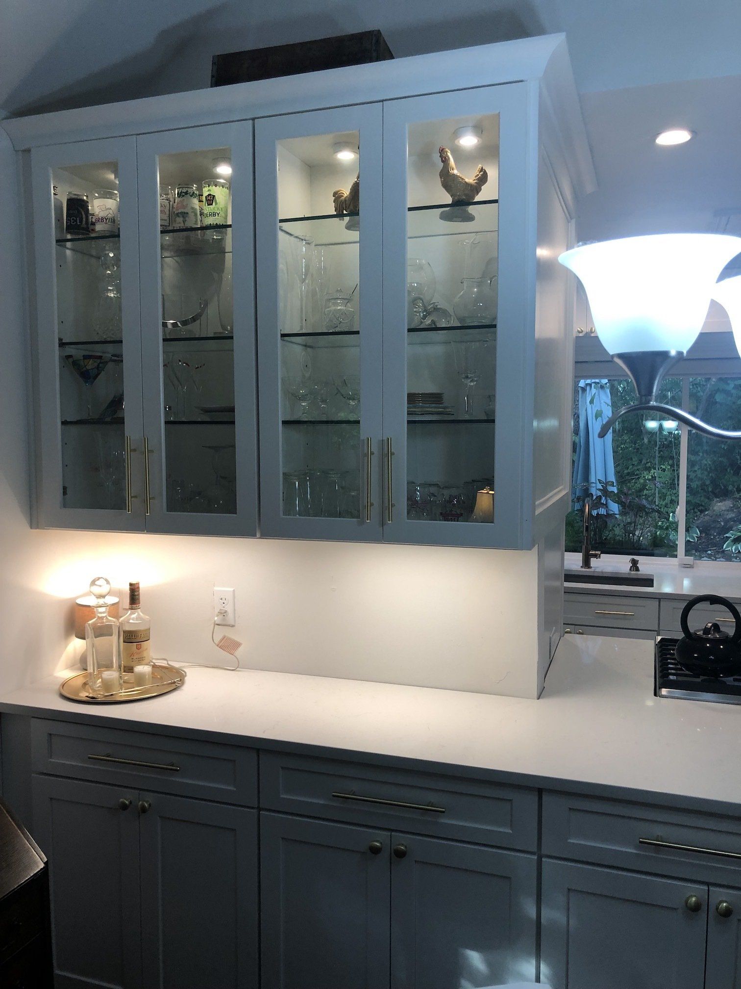 White kitchen cabinets with glass doors, illuminated shelf, dishes, and rooster figurines.