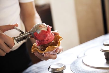 le mani di un gelataio che preparano una coppetta alla fragola