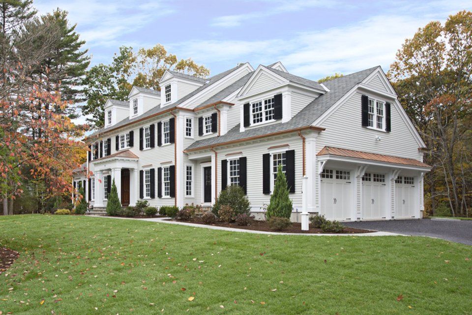 Large white colonial-style house with black shutters and a two-car garage, surrounded by autumn trees and lawn