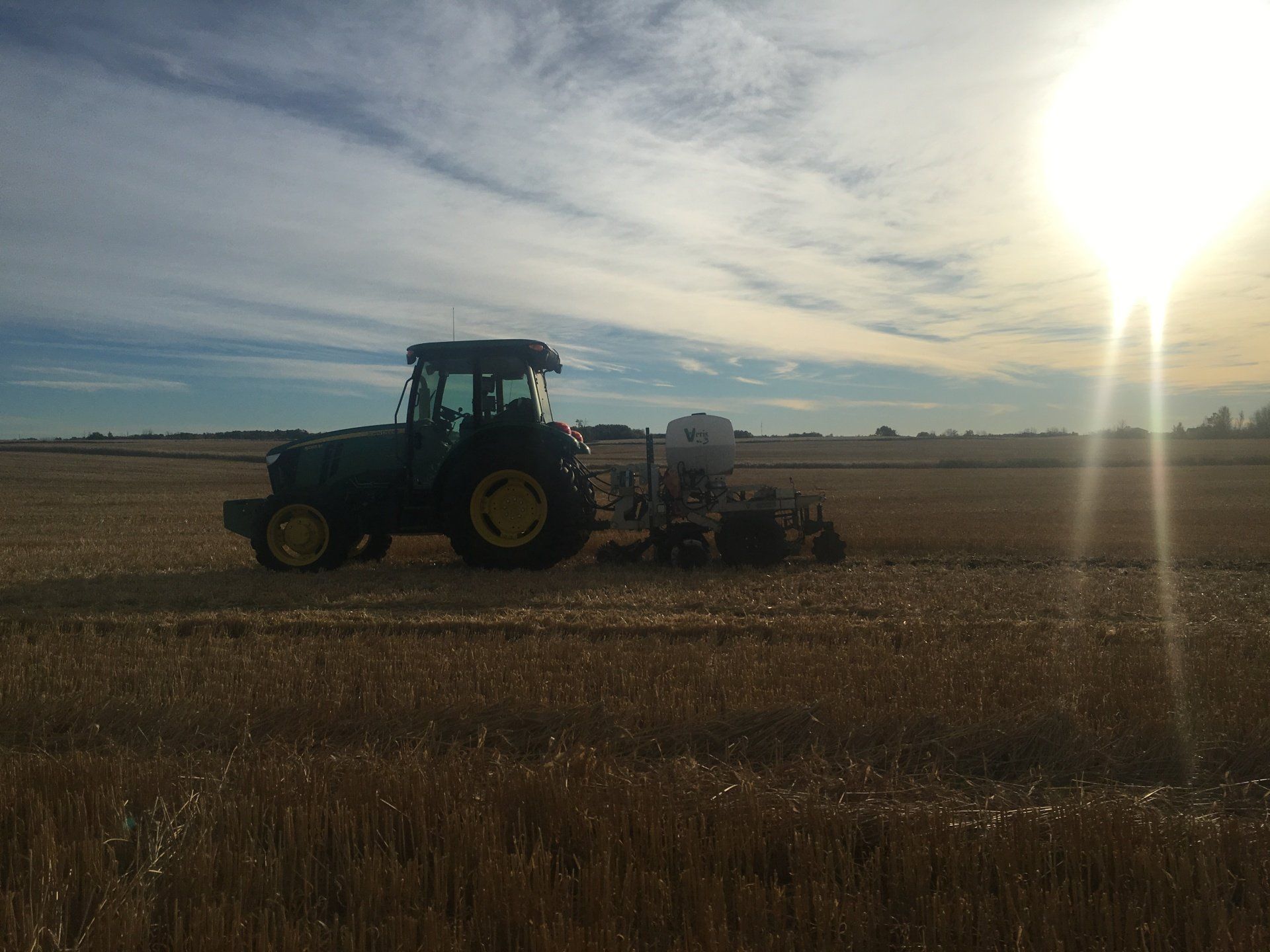 A green tractor pulling farm equipment through a field under a bright sun in a clear sky.