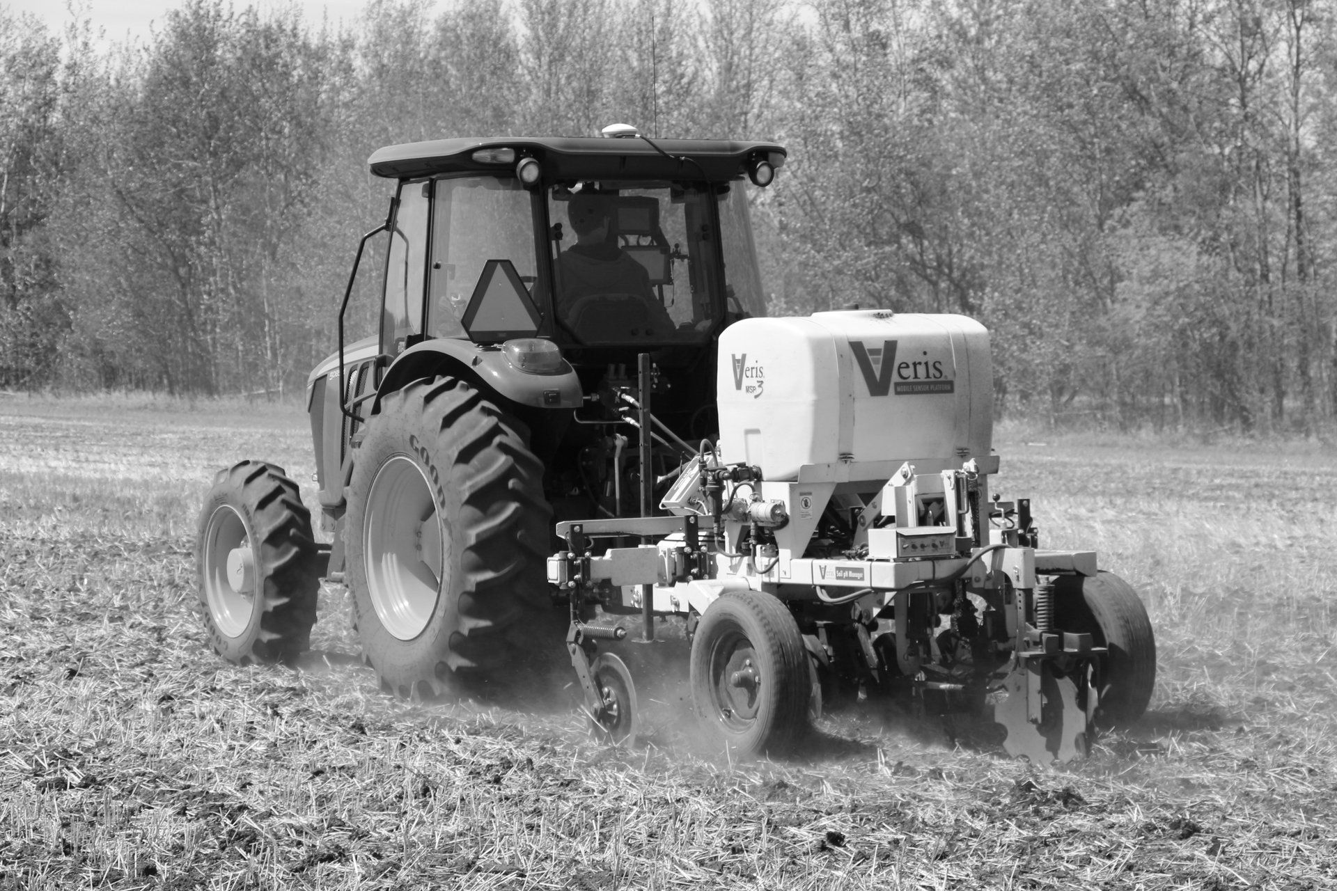A tractor driving across a field, pulling a Veris soil sensing unit to measure soil properties.