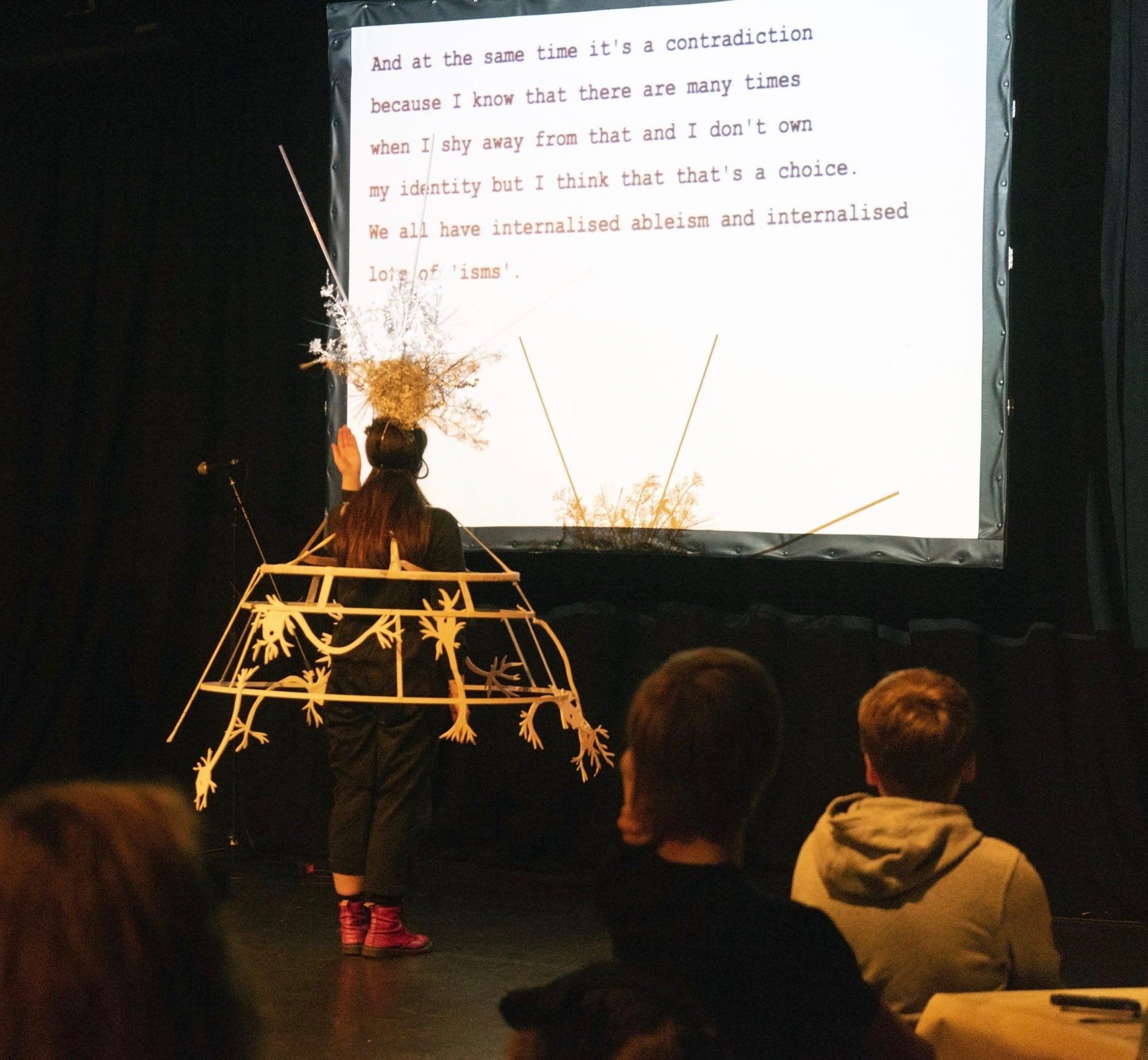 Character in white metal Crinoline faces large caption screen.