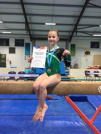 Gymnast sitting on a beam with a medal