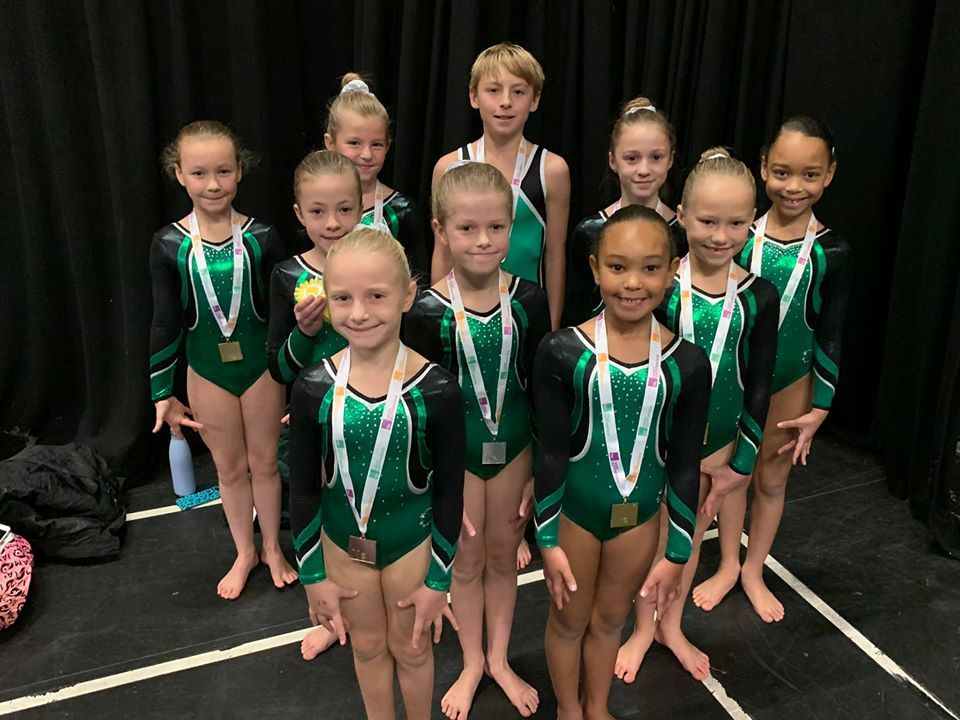 Gymnasts wearing medals, smiling and celebrating after a competition