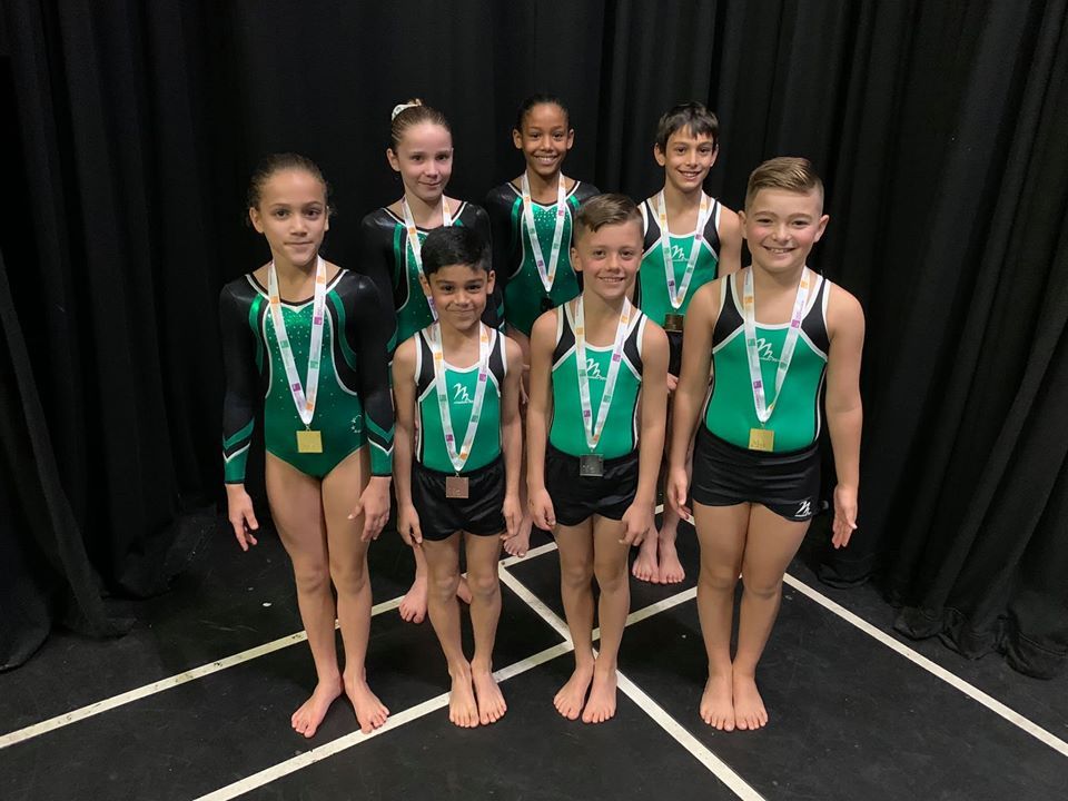 Gymnasts wearing medals, smiling and celebrating after a competition