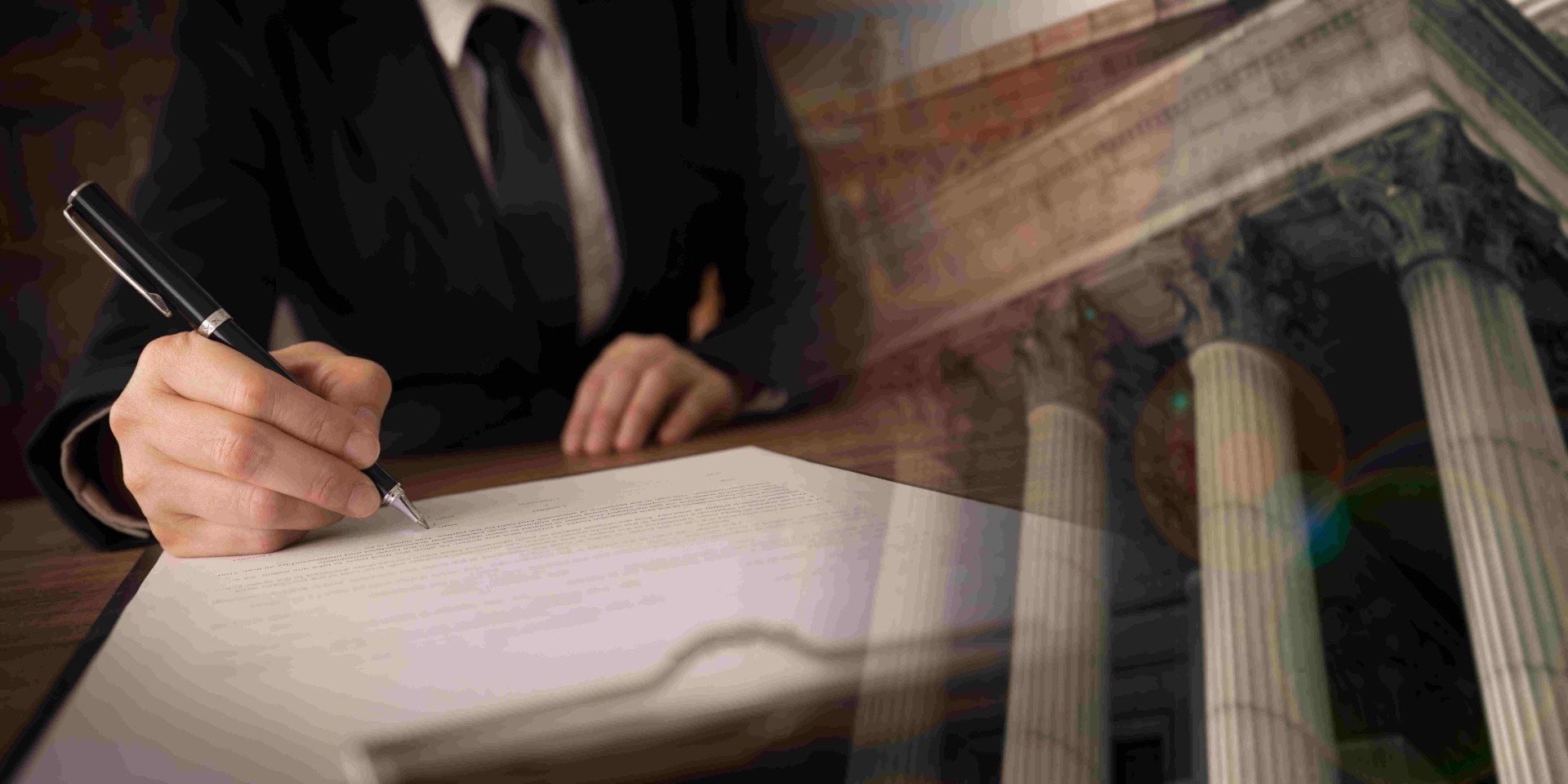 Ein Mann in Anzug und Krawatte schreibt auf ein Blatt Papier.