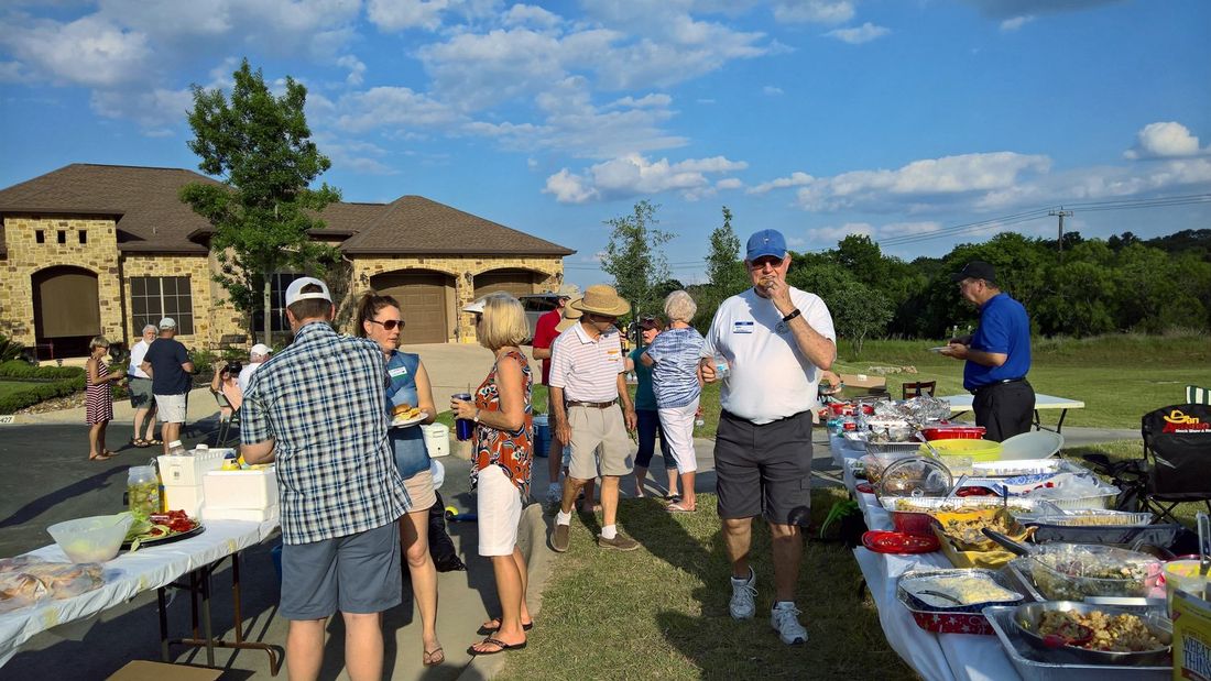 A group of people are standing around tables with food in front of a house.