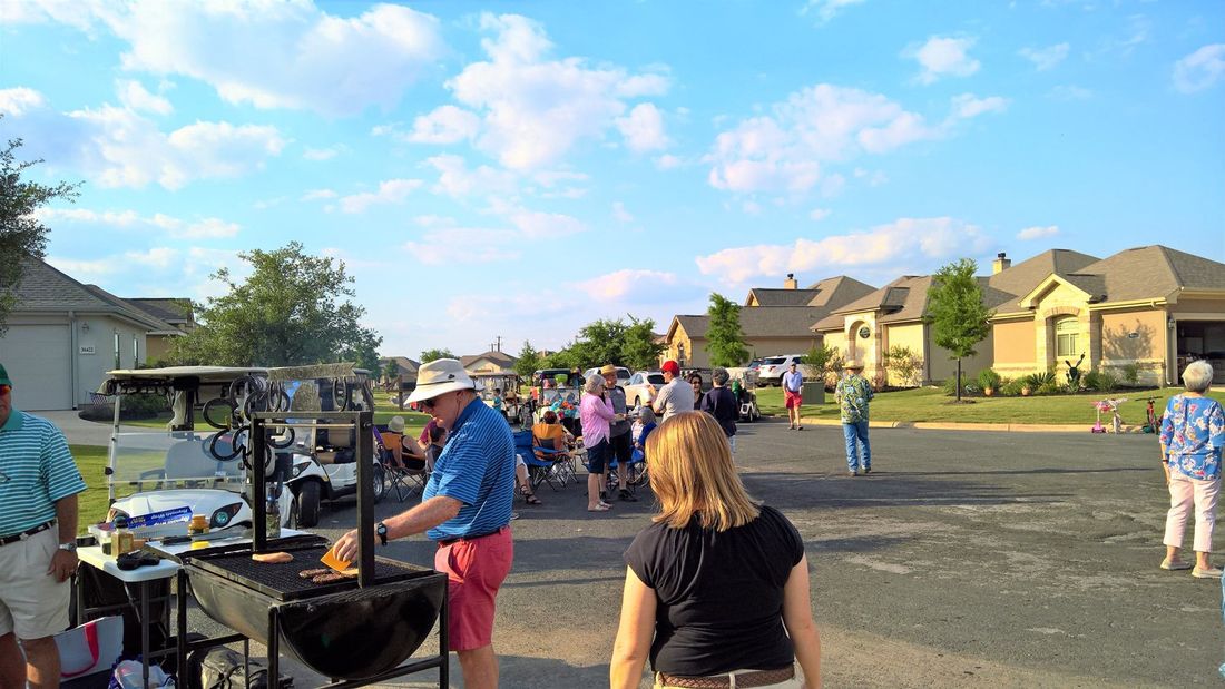 A group of people are standing around a grill in a parking lot.