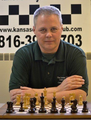 A man in a green shirt is sitting in front of a chess board