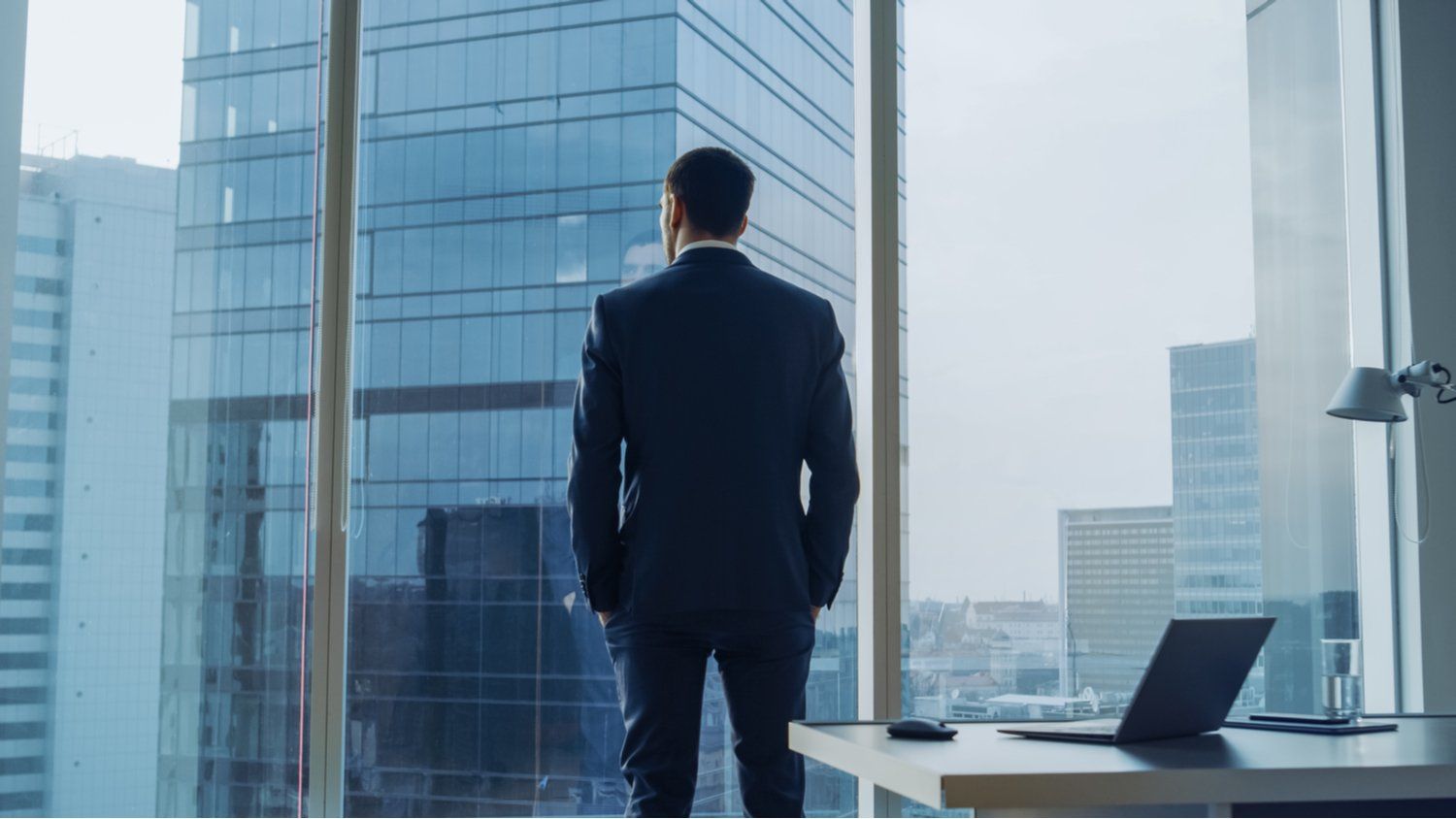 A businessman stood looking out a full floor window in a skyscraper