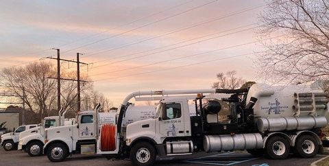 A row of vacuum trucks are parked in a parking lot.