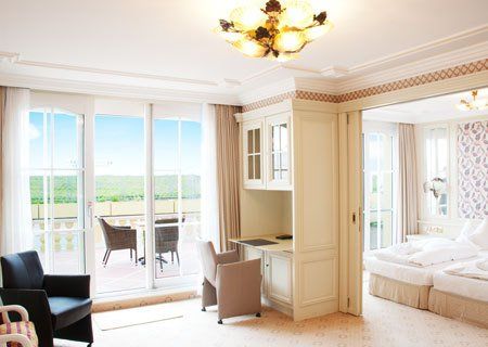 A hotel room with a bed , chairs , desk and sliding glass doors.