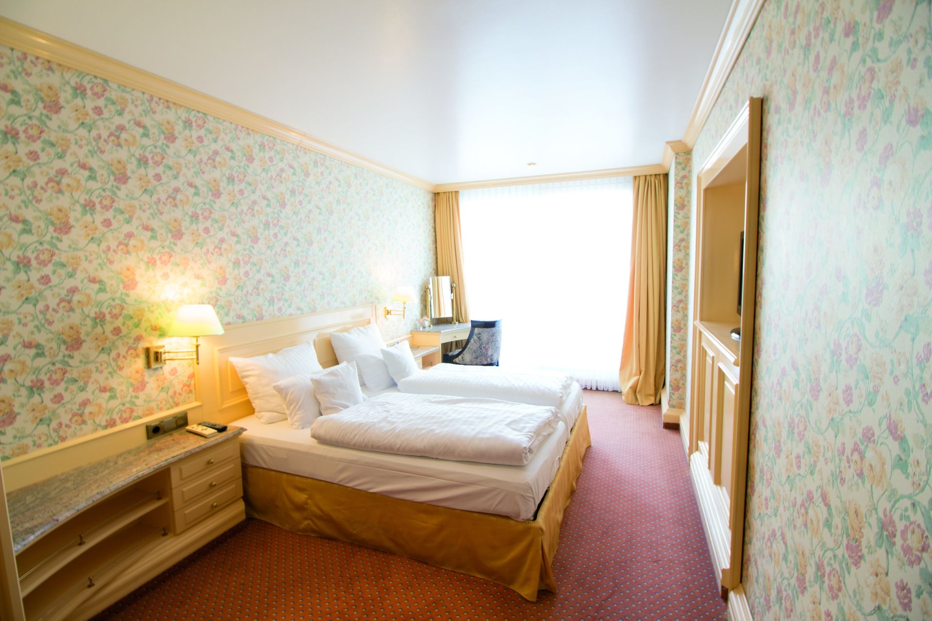 A hotel room with two beds and a floral wallpaper.