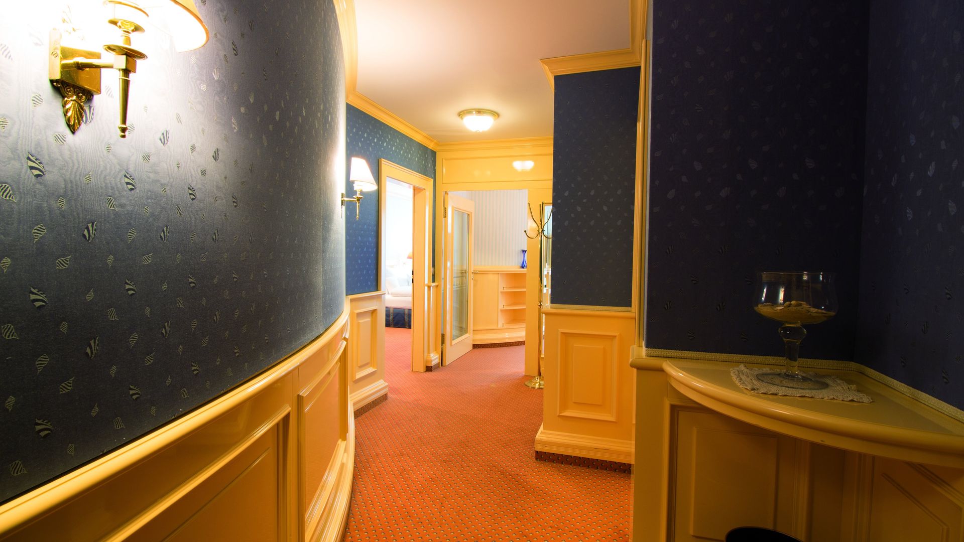 A hallway with a table in the corner and a lamp on the wall