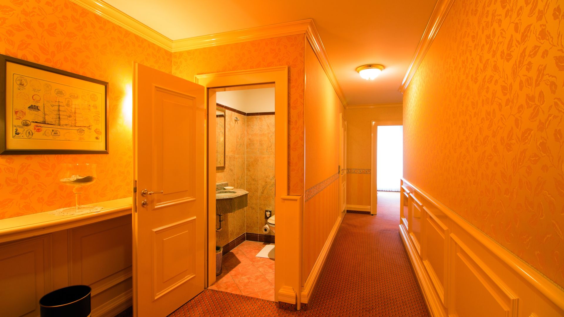 A long hallway leading to a bathroom and a sink in a hotel room.