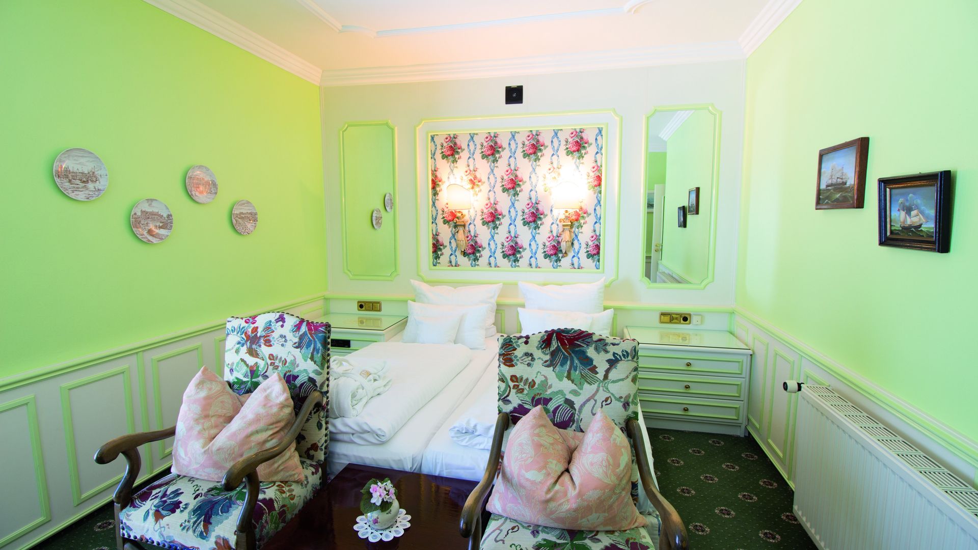 A bedroom with green walls , a bed , two chairs and a table.