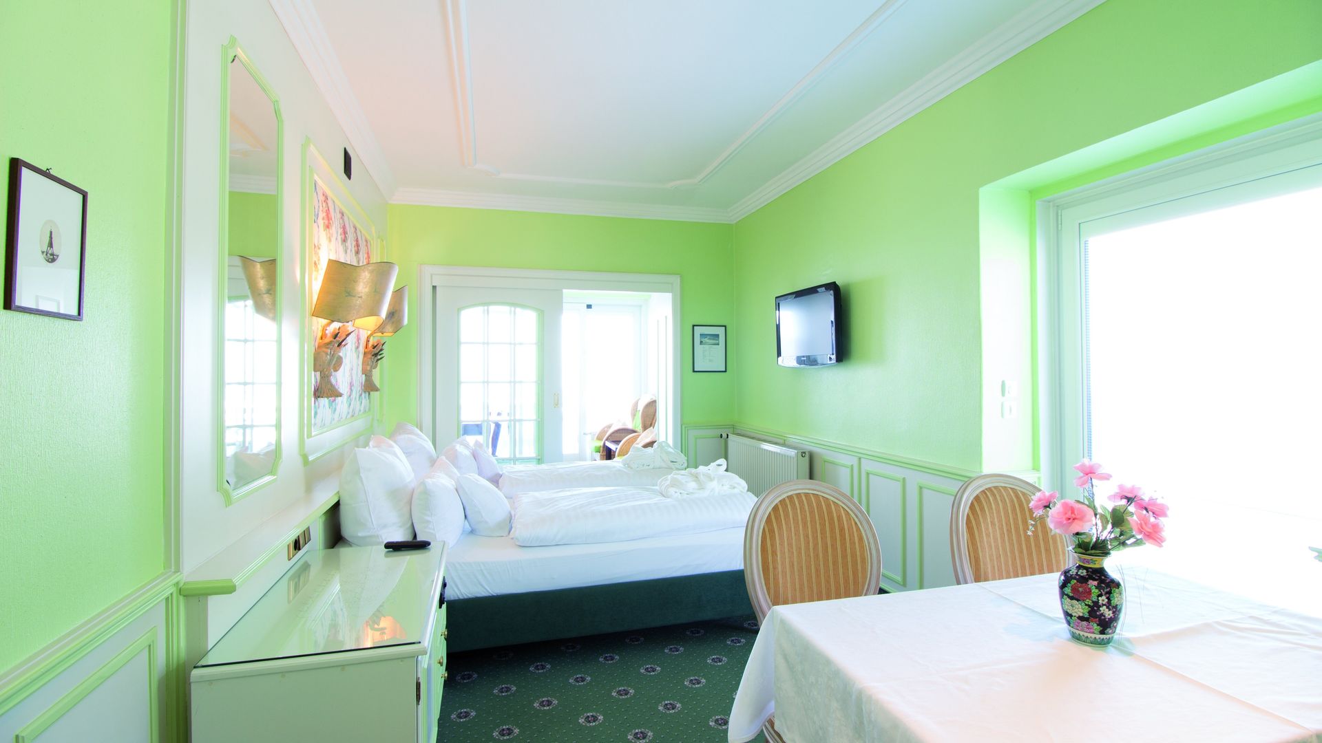 A hotel room with green walls , a bed , a table and chairs.