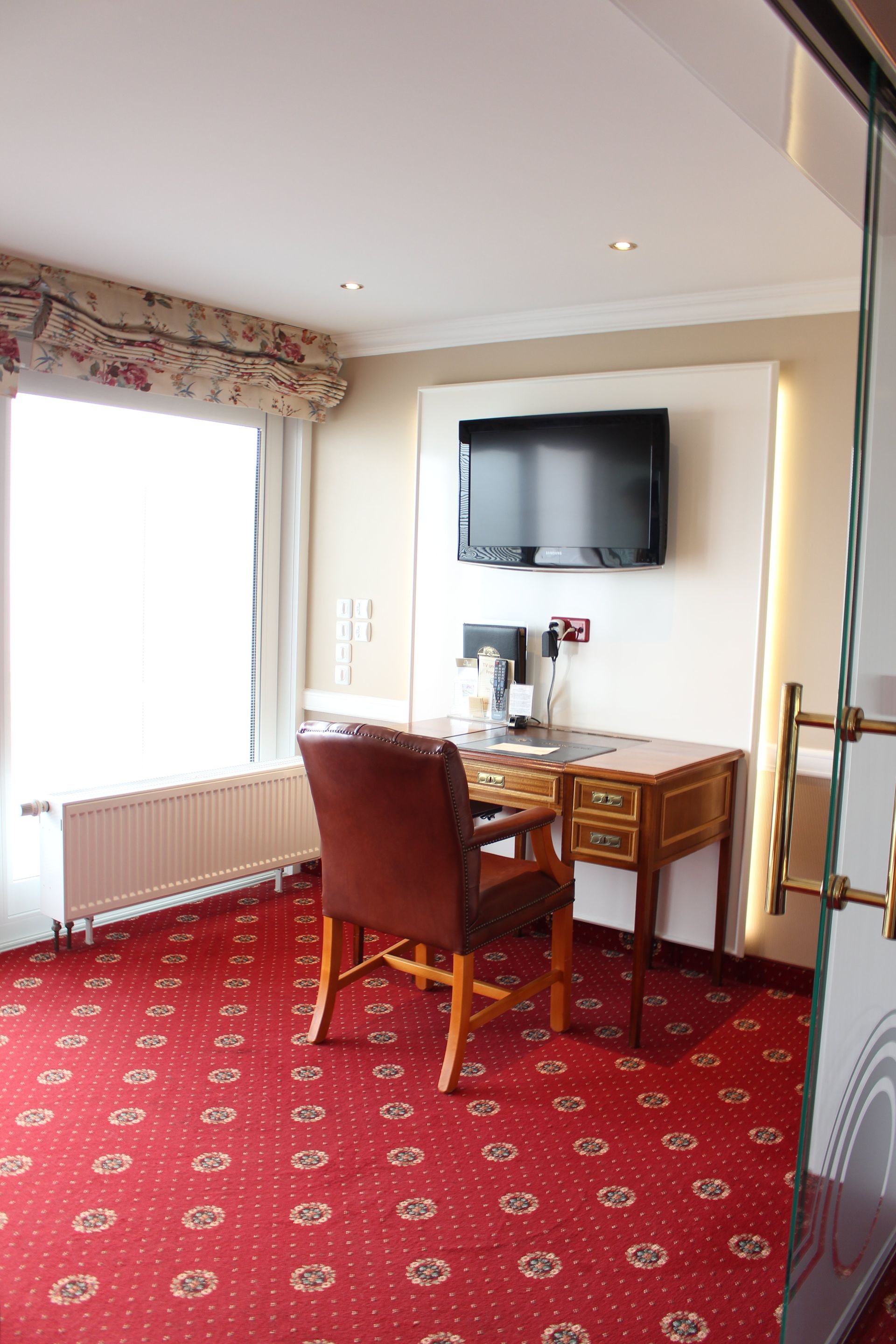 A hotel room with a desk and chair and a flat screen tv on the wall.