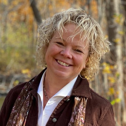 Dr. Erin wearing a brown jacket and a scarf is smiling for the camera.