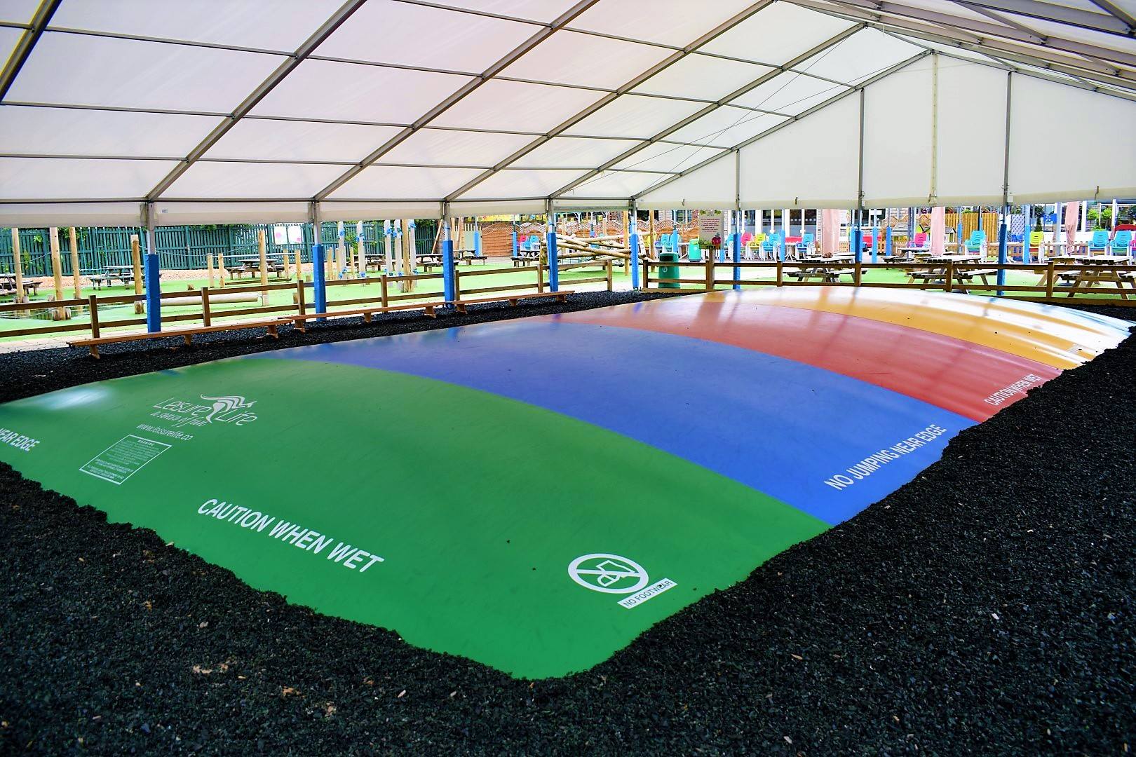 A rainbow colored trampoline is under a tent