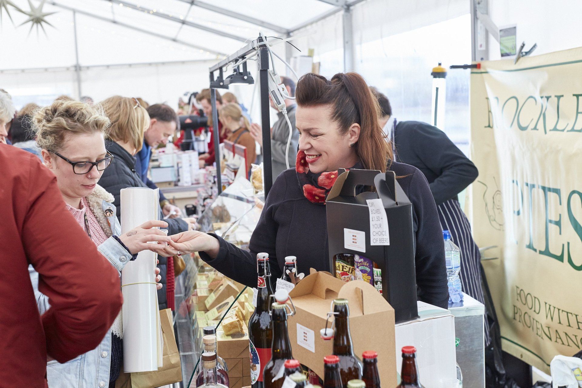 A woman is selling bottles of wine at a market.
