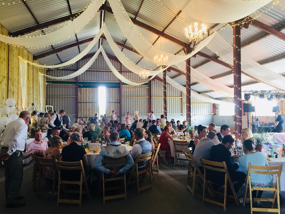 A large group of people are sitting at tables in a barn.