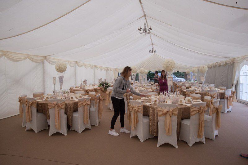 A woman is setting tables in a tent for a wedding reception.