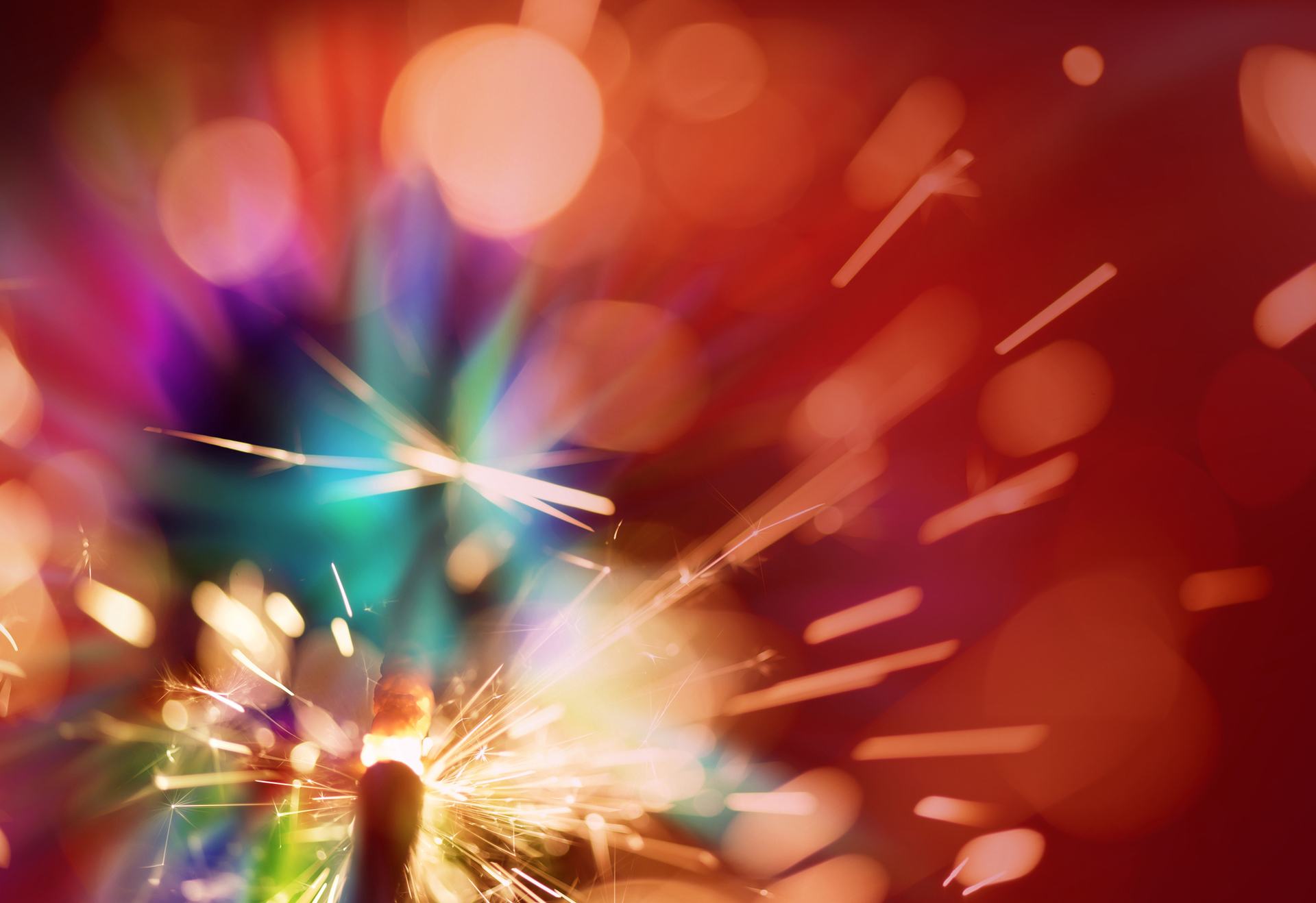 A person is holding a sparkler in front of a colorful background
