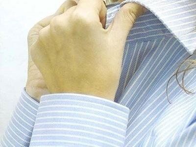 Primo piano di mani che reggono il colletto di una camicia a righe blu e bianche.