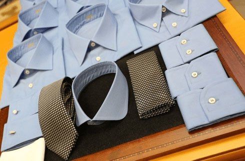 Camicie blu e cravatte disposte ordinatamente su un tavolo espositivo in legno.