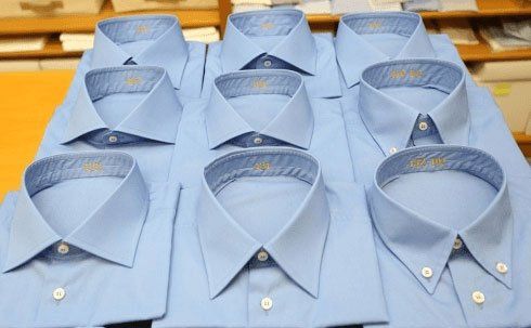 Camicie eleganti azzurre impilate e disposte ordinatamente su un tavolo.