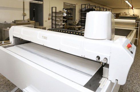 Grande macchina da stampa o da taglio industriale di colore bianco, presente in un'officina o in una fabbrica.