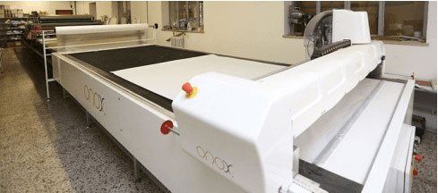 In un'officina si trova una grande macchina da taglio industriale di colore bianco, con piano di lavoro piatto e pannello di controllo a vista.