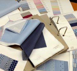 Campioni di tessuto nei colori blu, bianco e beige disposti su un campionario con raccoglitori ad anelli.