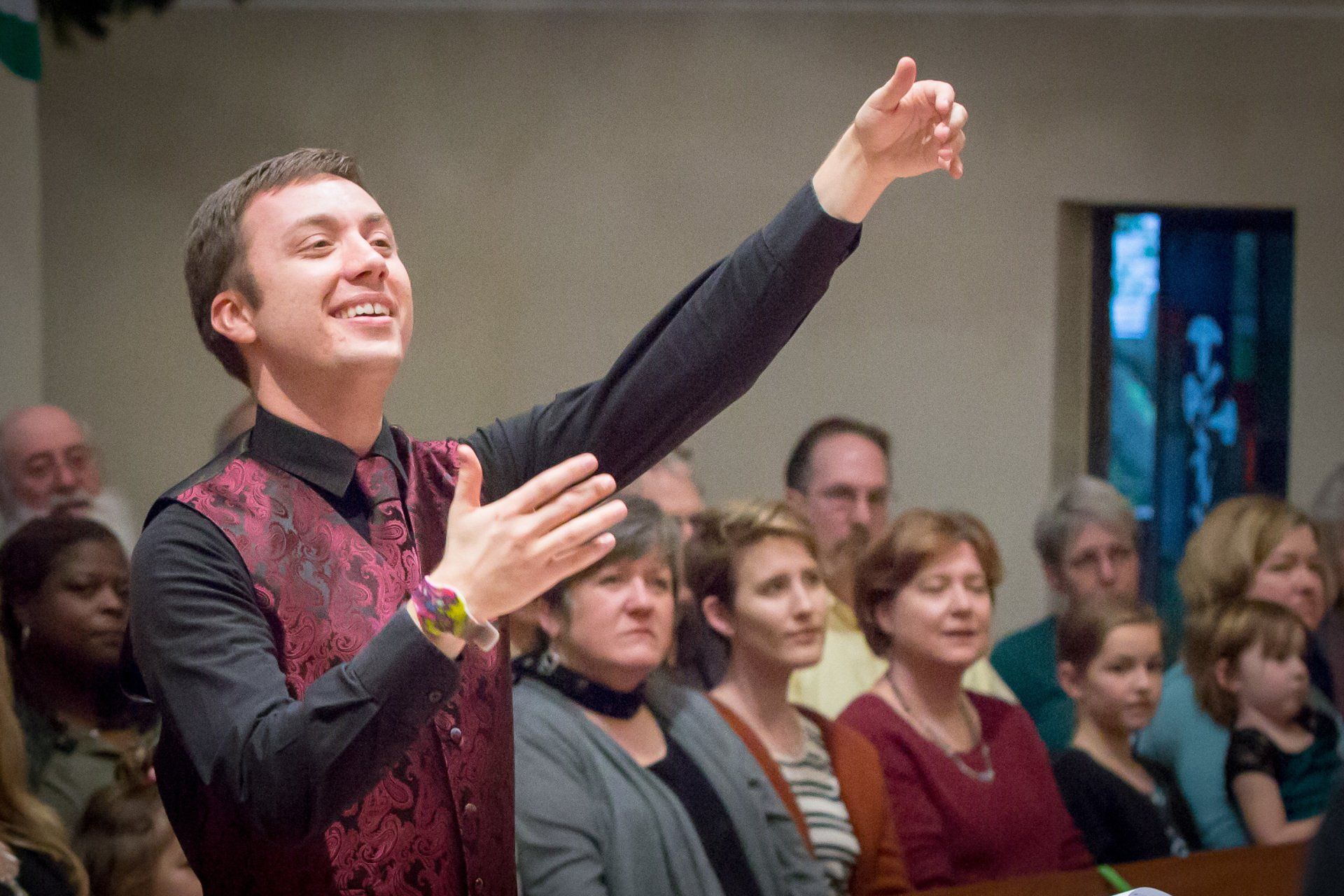 A man in a red vest is standing in front of a crowd of people.