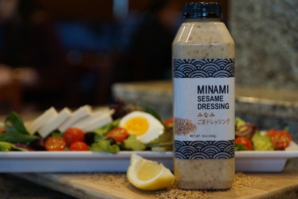 A bottle of minami sesame dressing is sitting on a cutting board next to a salad.