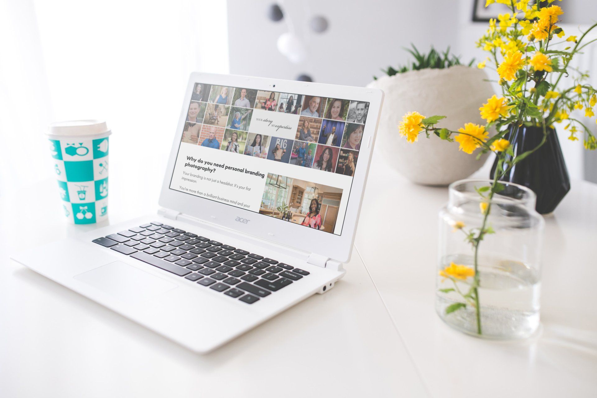 A laptop is open on a table next to a cup of coffee and a vase of flowers.