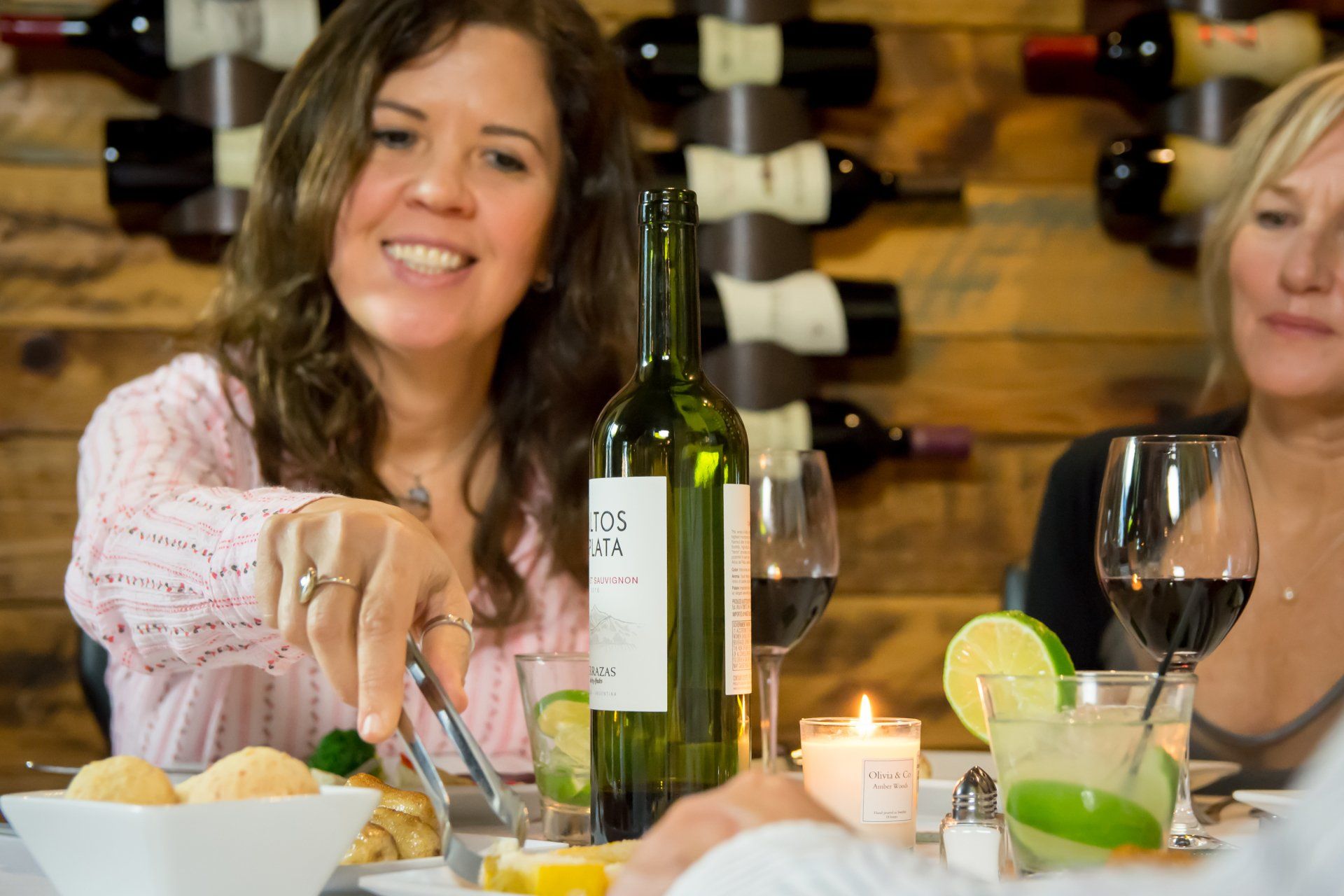 Two women are sitting at a table with a bottle of wine.