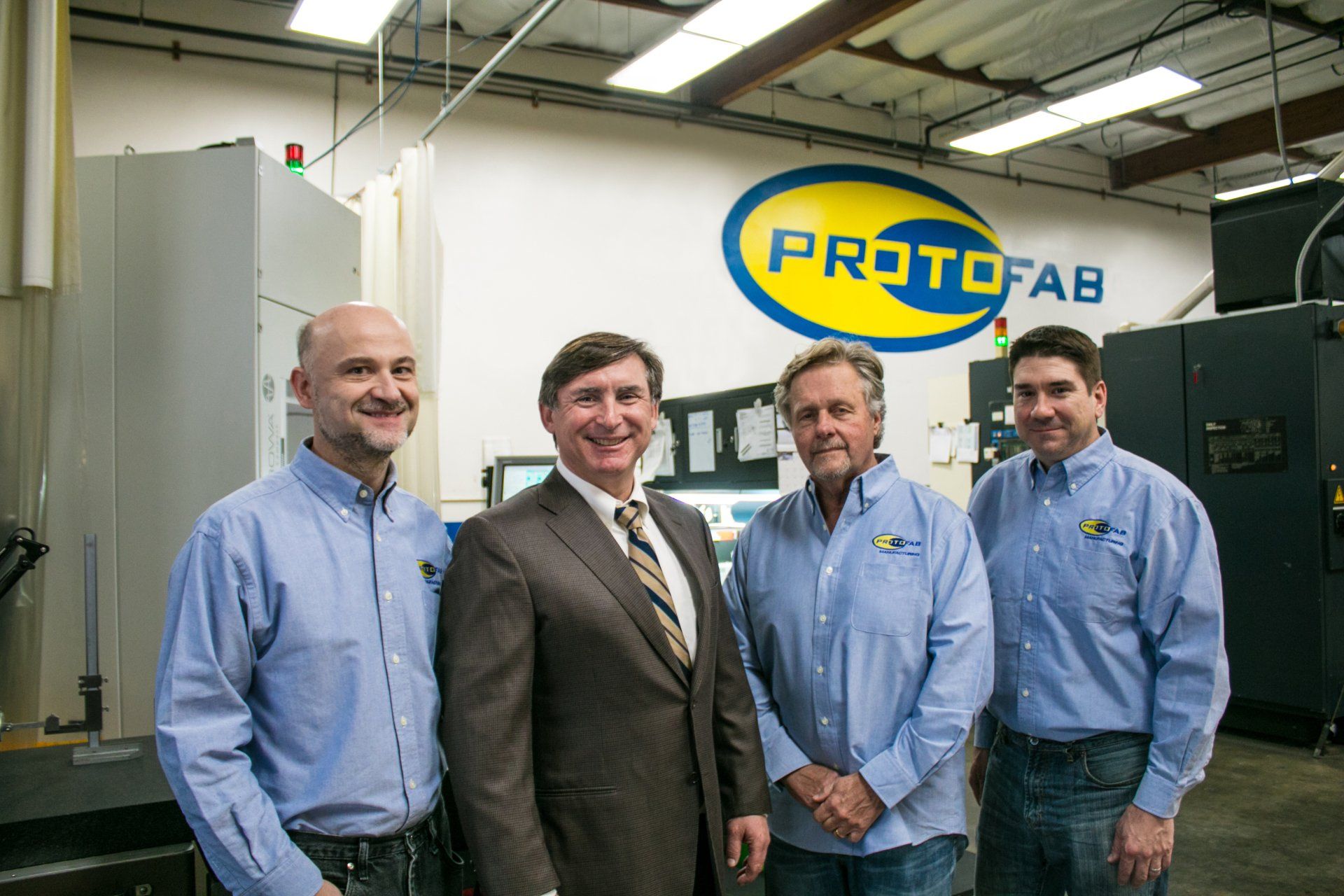 A group of men standing in front of a wall that says protofab