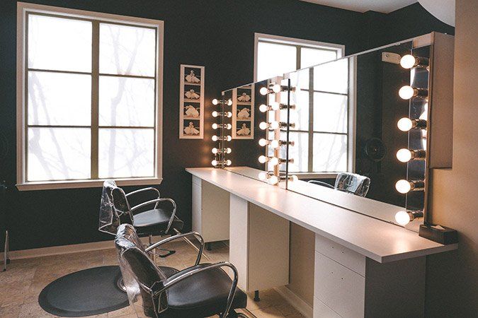 There are two chairs in the room with mirrors and lights.