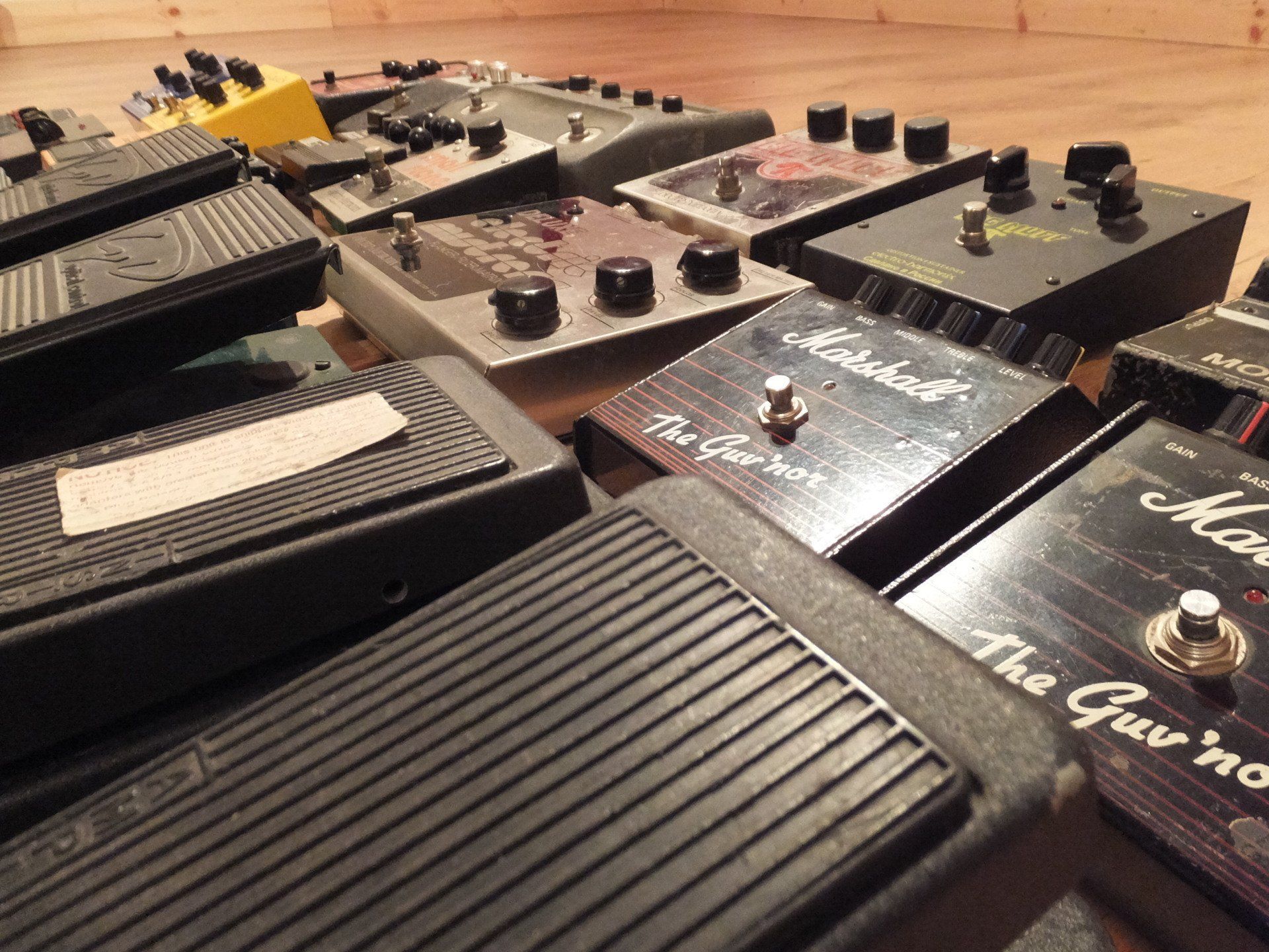 A close up of a dunlop wah-wah and the marshall govner with a selction of other pedals in the background