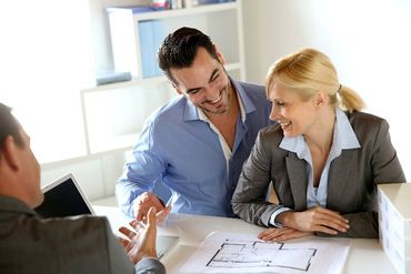 A man and woman are sitting at a table talking to a real estate agent.