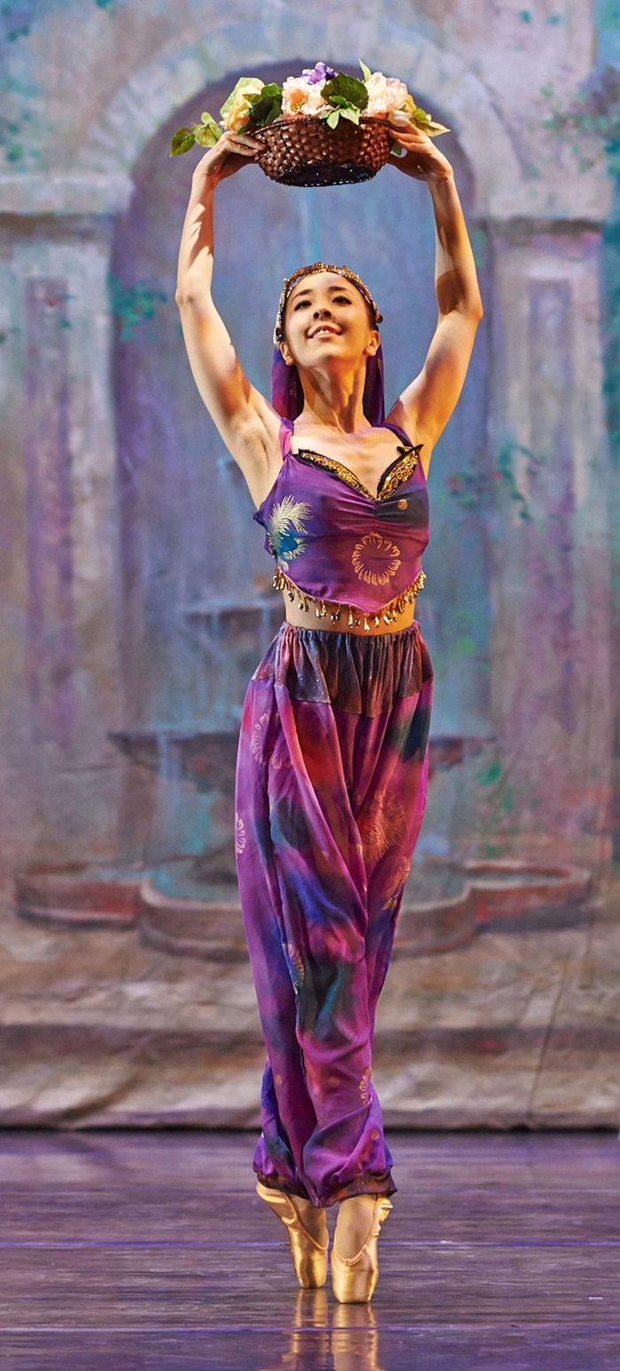Ballet dancer in a purple costume holding a flower crown overhead on stage
